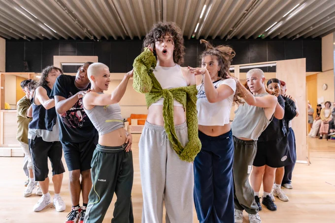 Performers stand in a V formation, at the center is Jo Foster who looks shocked