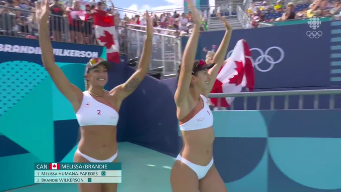 two beach volleyball athletes walking onto the sand with their arms raised and waving at the crowd