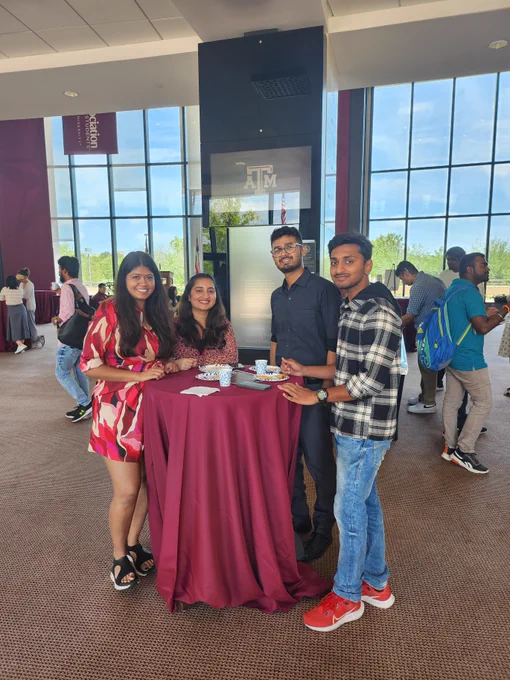 A group of students standing at a small round table with refreshments pose for a photo at the Texas A&M Association of Former Students building