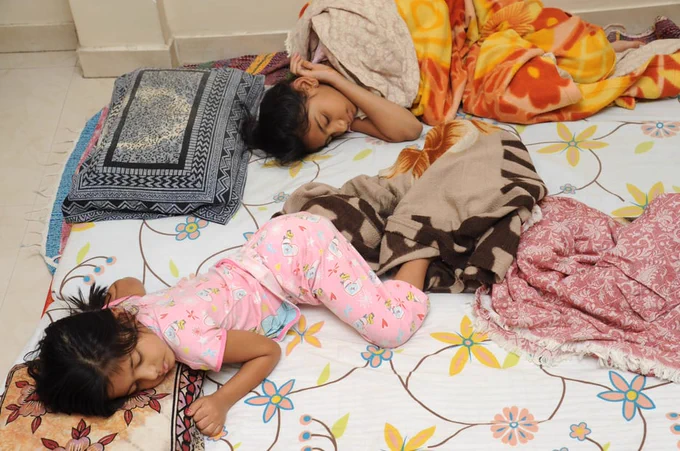 Two children lying on a blanket and pillows.
