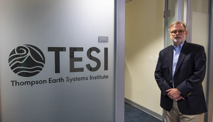 a man in a sportscoat is standing in an office doorway next to a frosted window with a round logo and the letters TESI