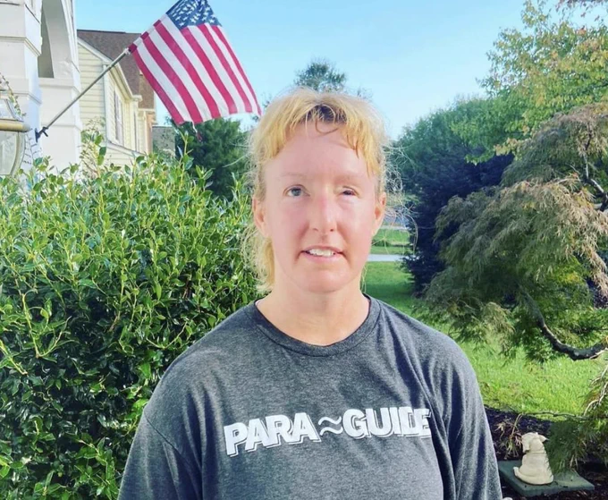 Julie smiles while wearing a Para Guide shirt in front of her home; an American flag flies in the background