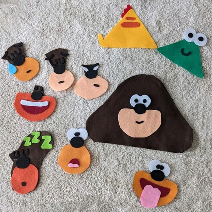 Cut out felt Hey Duggee masks, with different facial expressions, on a carpet. 