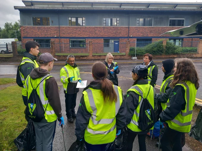 Police scotland youth volunteers are standing outside speaking to staff from the neighbourhood regeneration team before a litter picking event. 