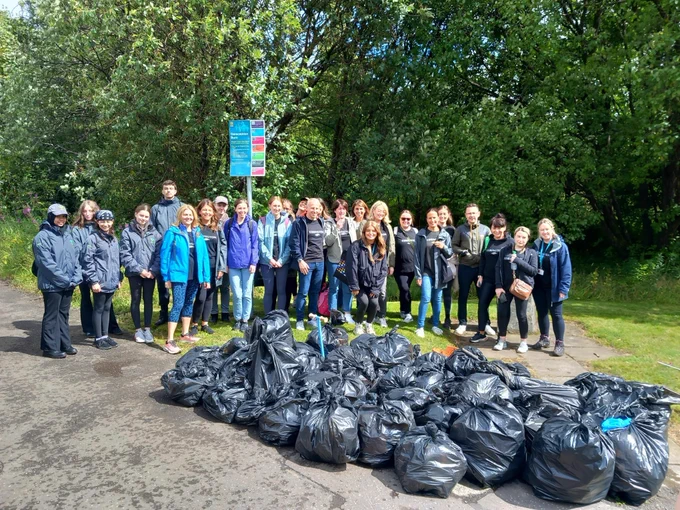 police scotland youth volunteers are standing outside with numerous black bin bags filled with rubbish after a litter picking event. 