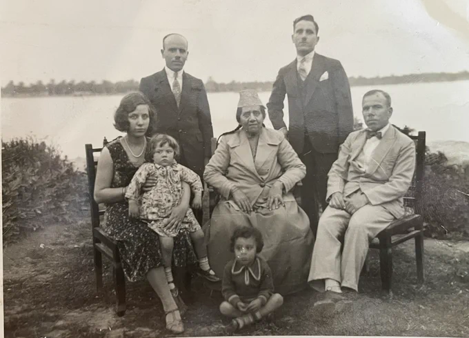 A black and white photo of the Saleh family sitting and standing in front of the Shatt Al Arab River.