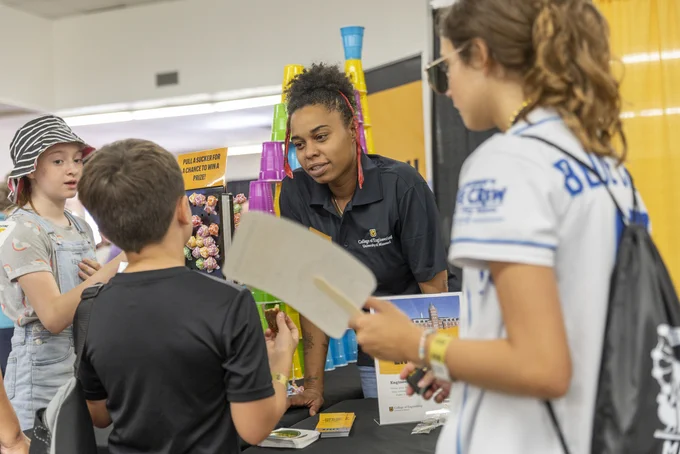 A woman in a Mizzou polo talks to a younger child. 