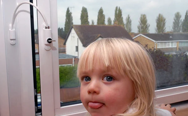Image shows a child's face in front of a window which is partially open. The window is being prevented form opening any further due to the presence of a window restrictor. 