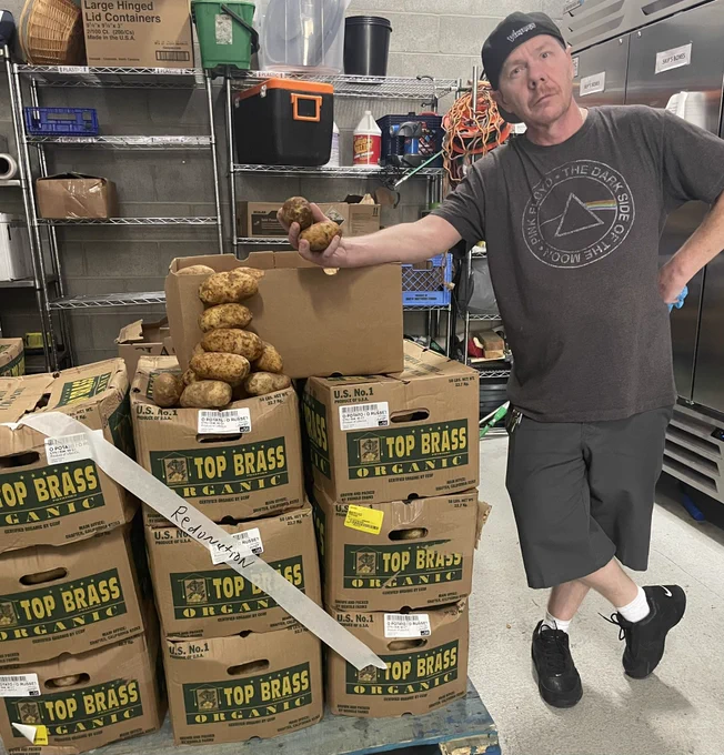 A man stands next to boxes of potatoes
