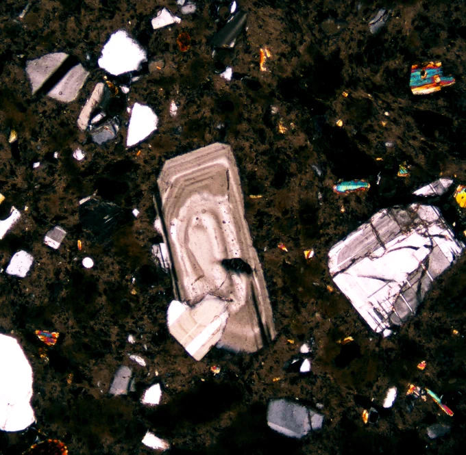 Heavily zoned plagioclase phenocryst in a bed of darker ground mass. The bottom left of the plagioclase lathe has a wee heart shaped overgrowth.
