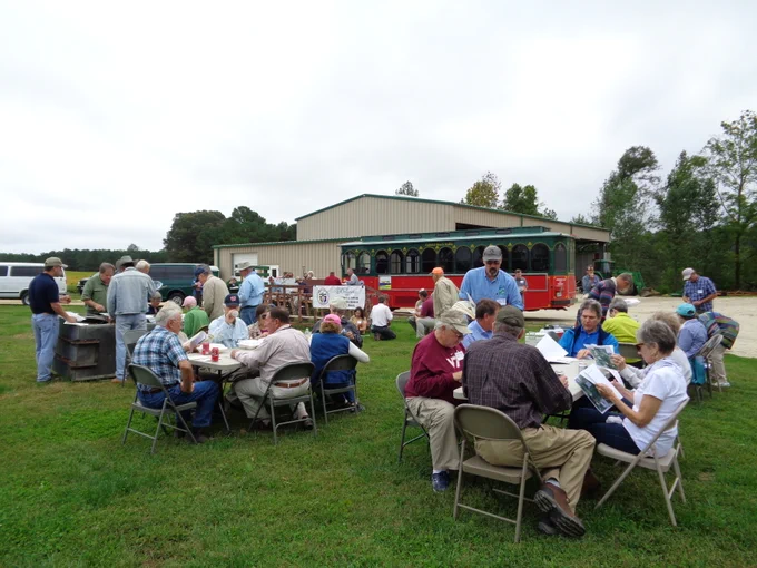 Groups of people eating lunch sitting at round tables in a field. 