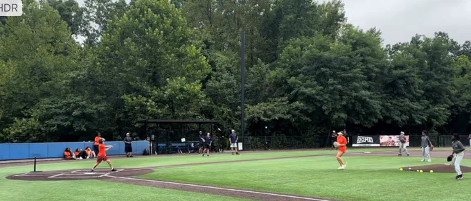 A camp participant hits a baseball into the outfield of a baseball field.