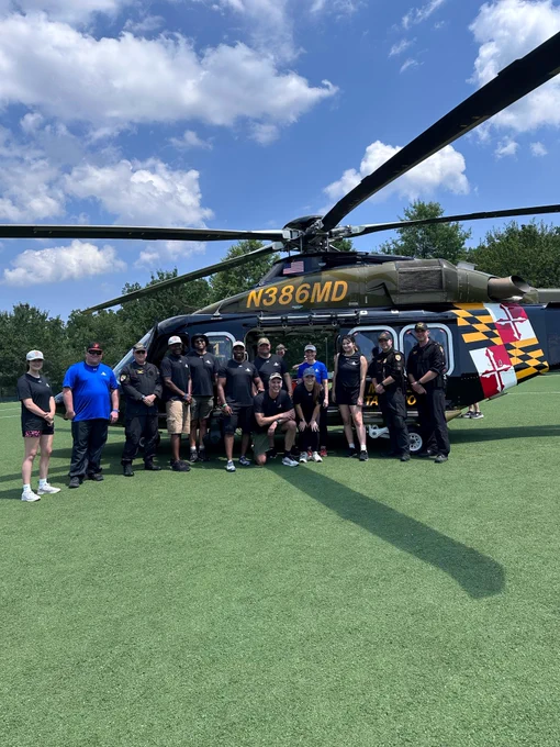 A group of law enforcement officers stand in front of a Maryland State Police helicopter.