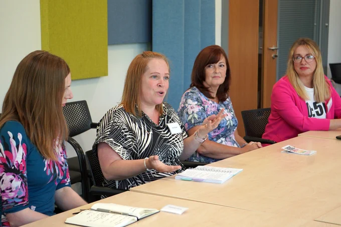 Image of four women from 50:50 Parliament seated at table. The woman seated second from the left speaks across the table, as the others look on. 