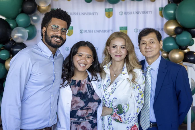 A rush cardiac perfusion student stands with family members in front of a banner with "Rush University" logo, surrounded by balloons. They are smiling and dressed in smart casual attire.