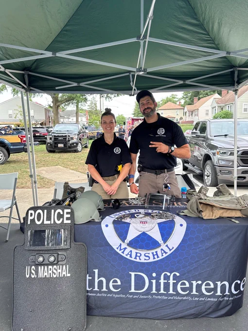 Two Deputy U.S. Marshals pose in front of a recruitment display.
