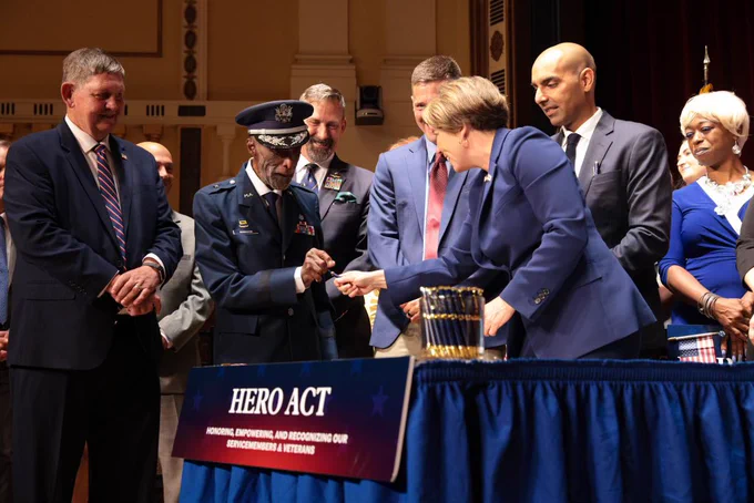 Governor Healey handing pen to general Woody Woodhouse.