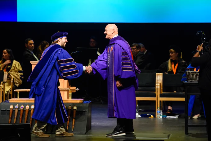 President Clements shaking hands with a doctoral degree recipient as they cross the stage.