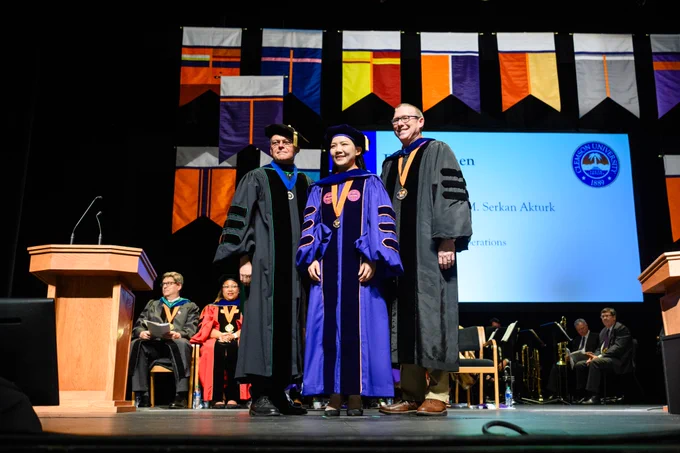 Three people standing on a stage and posing for a photo during the doctoral commencement ceremony.