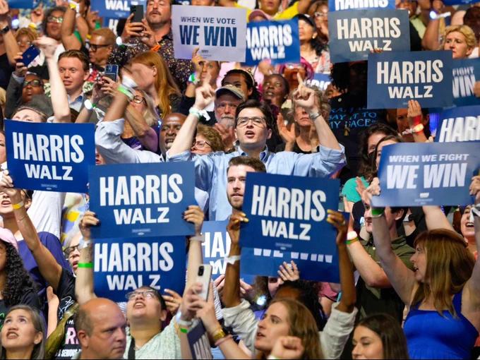 Event attendees cheering and holding blue and white signs that read: Harris-Walz.
