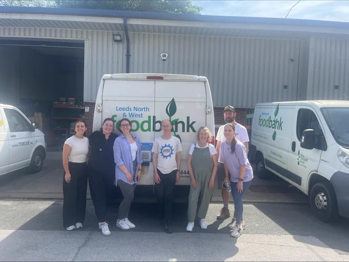 Group of IMA team members stood in front of a Leeds North and West Foodbank van, with one of the team from the Trussell Trust