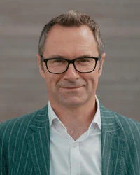 Headshot of Professor Darren Dixon from Oxford University, wearing a white shirt, striped blazer, and black-rimmed glasses