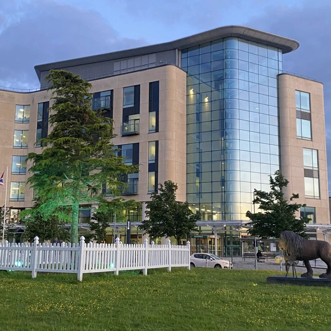 A large stone and glass building with a tree and lion statue in the forefront