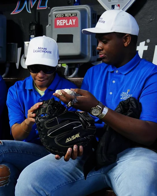 A Miami Lighthouse teen student with vision impairment explores a baseball glove with the help of a Miami Lighthouse volunteer.