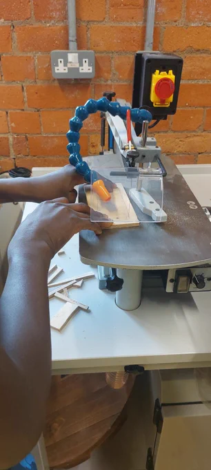 A person operates a machine, skilfully shaping a piece of wood in a workshop environment.