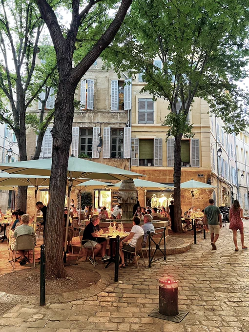Aix-en-Provence. People dining under awnings. Bollard in the foreground.
