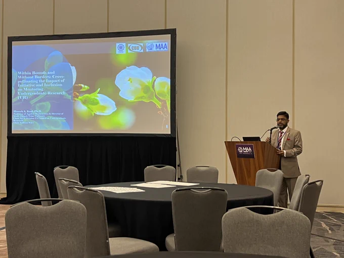 Photo of Dr. Kazi next to the screen projecting his presentation