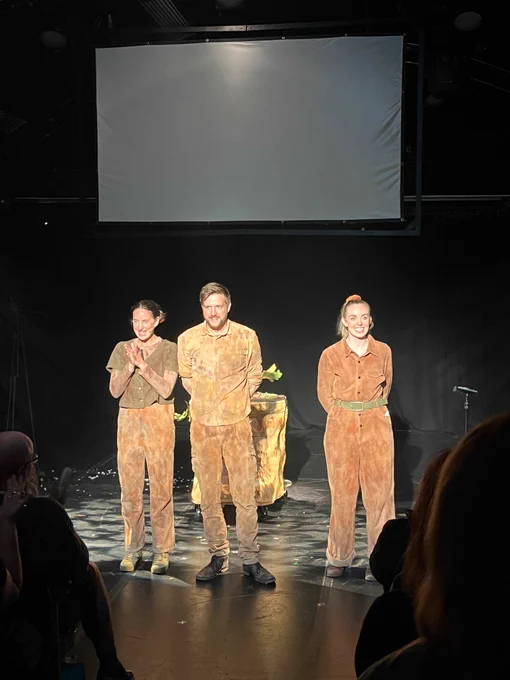 on a stage, three performers are standing facing the audience.
