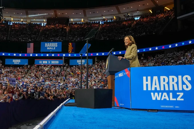 Vice President Kamala Harris stands behind a podium looking out at a full arena of supporters.