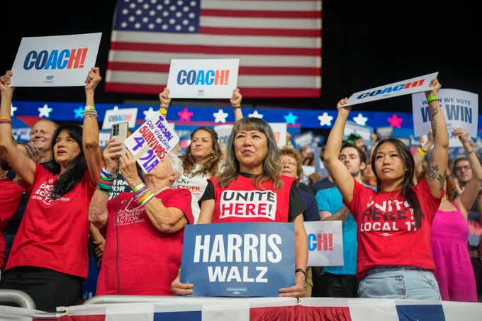 A crowd of Vice President Kamala Harris and Governor Tim Walz supporters hold signs that say "COACH!", "HARRIS WALZ", "KAMALA", and "WHEN WE VOTE, WE WIN".