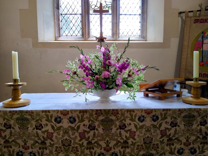 A photo of St Michael and All Angels Church, Pinhoe Devon, showing the altar with candles and a display of flowers.