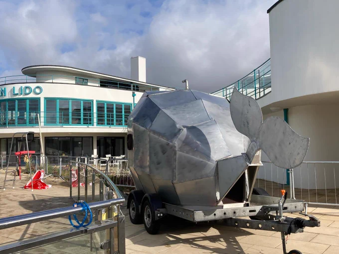 Big metal Whale, seen from the tail end, in front of an art deco pavilion signed Lido