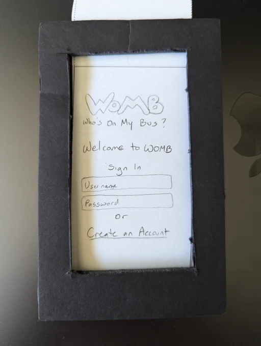 Cardboard frame around a narrow strip of paper with a hand drawn login screen for WOMB: Who's on my bus? 