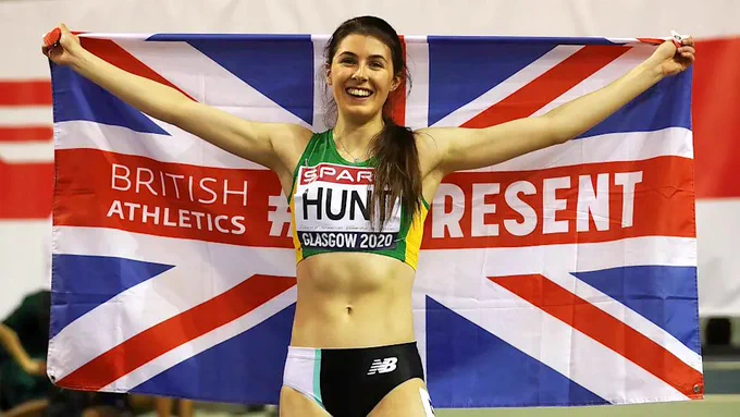 Runner Amy Hunt in running gear holding a British flag up behind her in triumph.