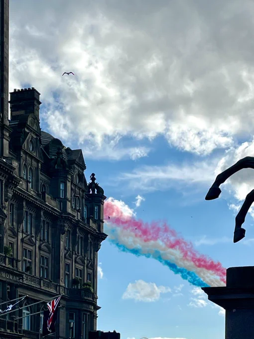 Blue sky and classic architecture. Up in the sky, three streams of colored jet trail, pinkish red, yellow, blue.