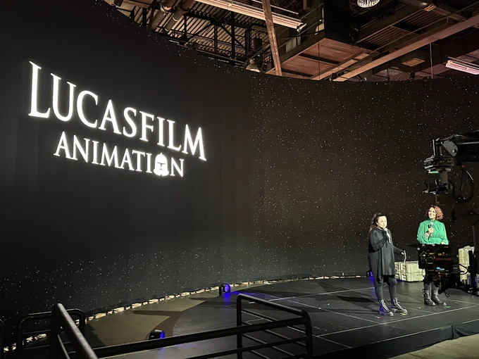 Athena Portillo, in an all-black ensemble, is joined by Vanessa Marshall in a green top in front of the Lucasfilm Animation symbol on ILM StageCraft.