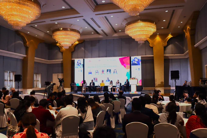 Panelists engage in a lively discussion at the Nepal Youth Summit 2024, held under the theme 'Investing in Youth for Prosperous Nepal.' The stage features six speakers seated in front of a large screen displaying the event’s title, their photos, and names. A participant sits attentively in the foreground, listening to the discussion. The backdrop is adorned with logos of various organizations supporting the Summit of the Future.