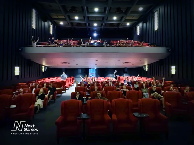 A movie theater hall, with people sitting in the seats. They are smiling, and some have their hands in the air. 