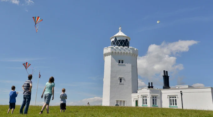 Family flying kites next to a white-washed lighthouse. Copyright National Trust