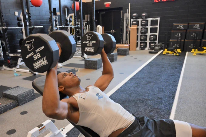 Jayden Pierre lifting fifty-five pound dumbbells in the weight room