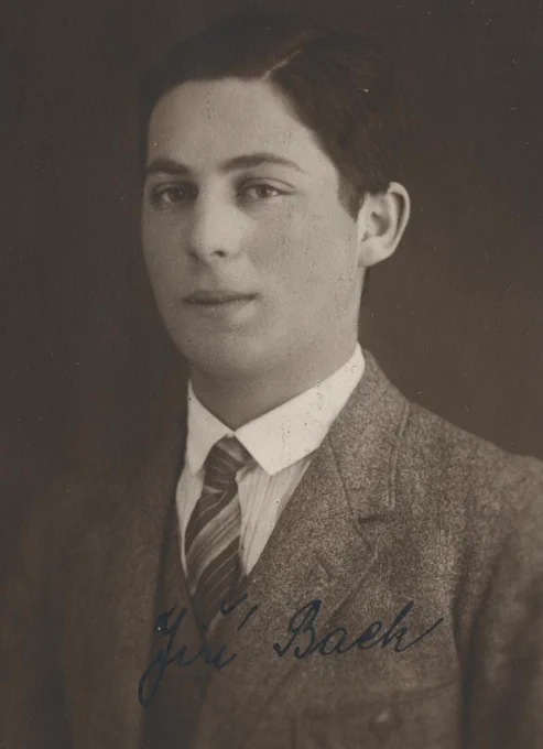 Vintage black and white portrait of a young man in a suit and tie. The photograph features a subtle, textured background and the individual has a slight, indirect gaze. There is a handwritten signature at the bottom.
