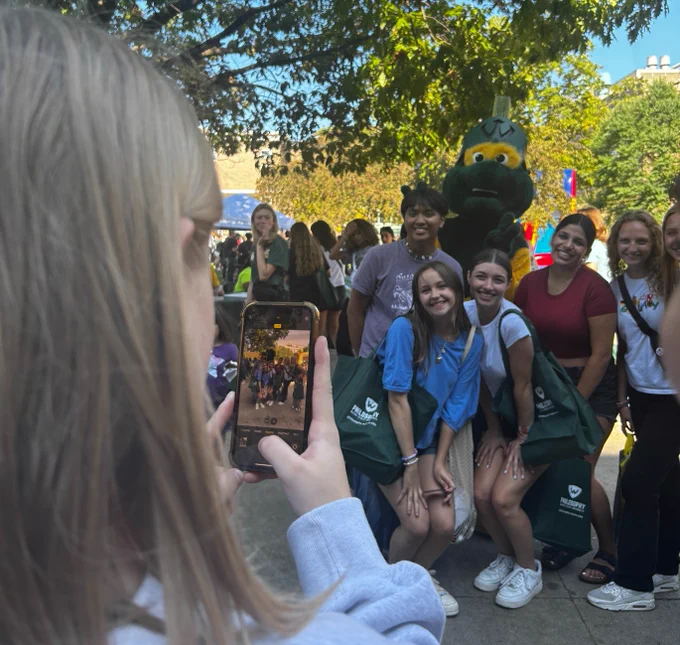 A girl takes a photo of a group of students posing with W.