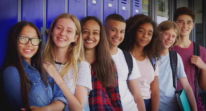 A line of 7 students stands in front of blue lockers. 