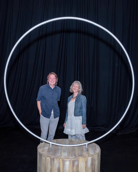 Playwrights Boff and Sarah stood behind an upright circle on the black set of Sanctuary 