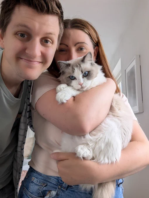 Jordan and Ruth Barrett smile at the camera cuddling their rescue cat Dolly. Dolly is a grey, chocolate and white Ragdoll cat with bright blue eyes.