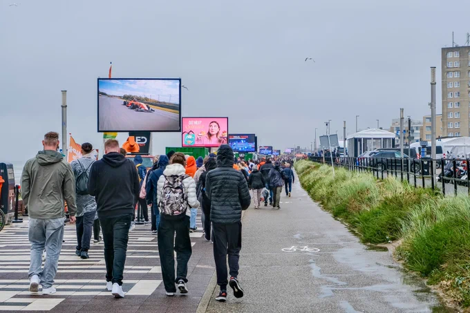 Crowds of people wearing rain gear walk, cycle, and ride the bus and train during the Dutch Grand Prix on a rainy day in Zandvoort.